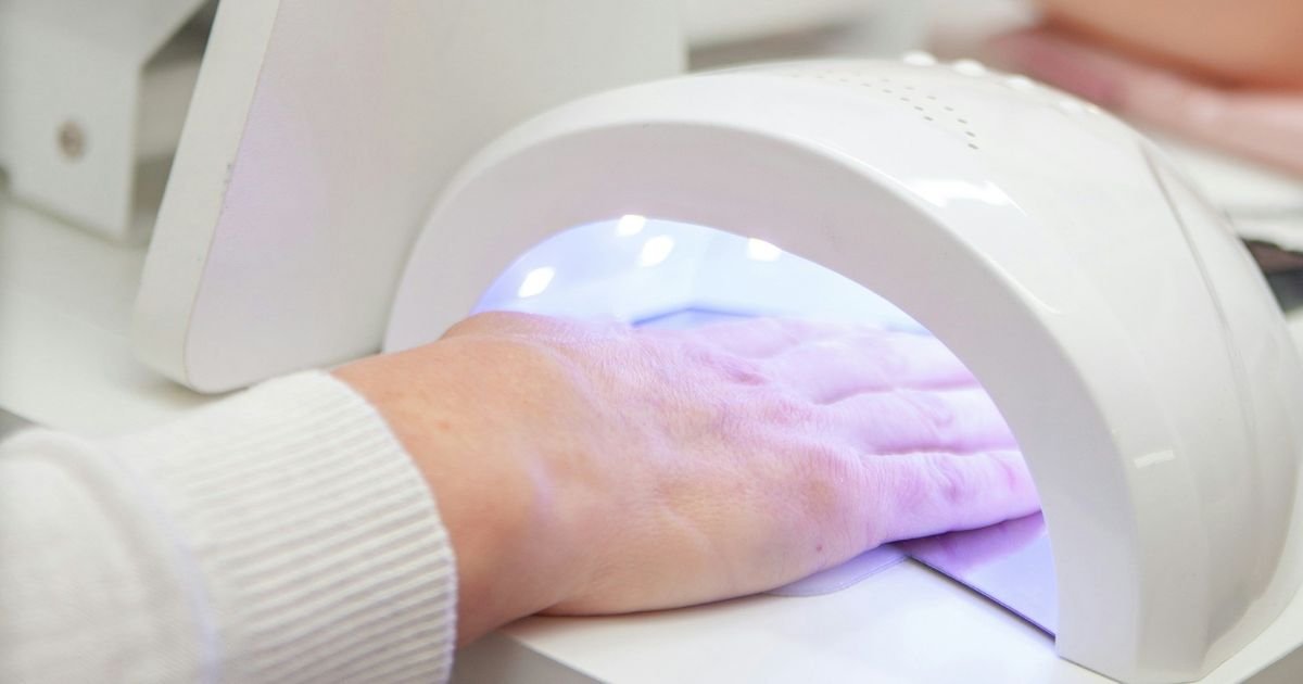 Cliente com a mão em cabine de led UV em estúdio de Nail design
