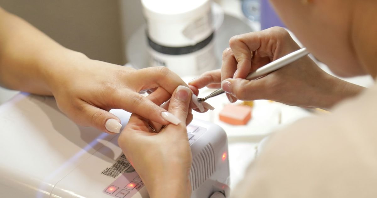 Nail designer aplicando gel para alongamento de unhas em cliente com cabine LED